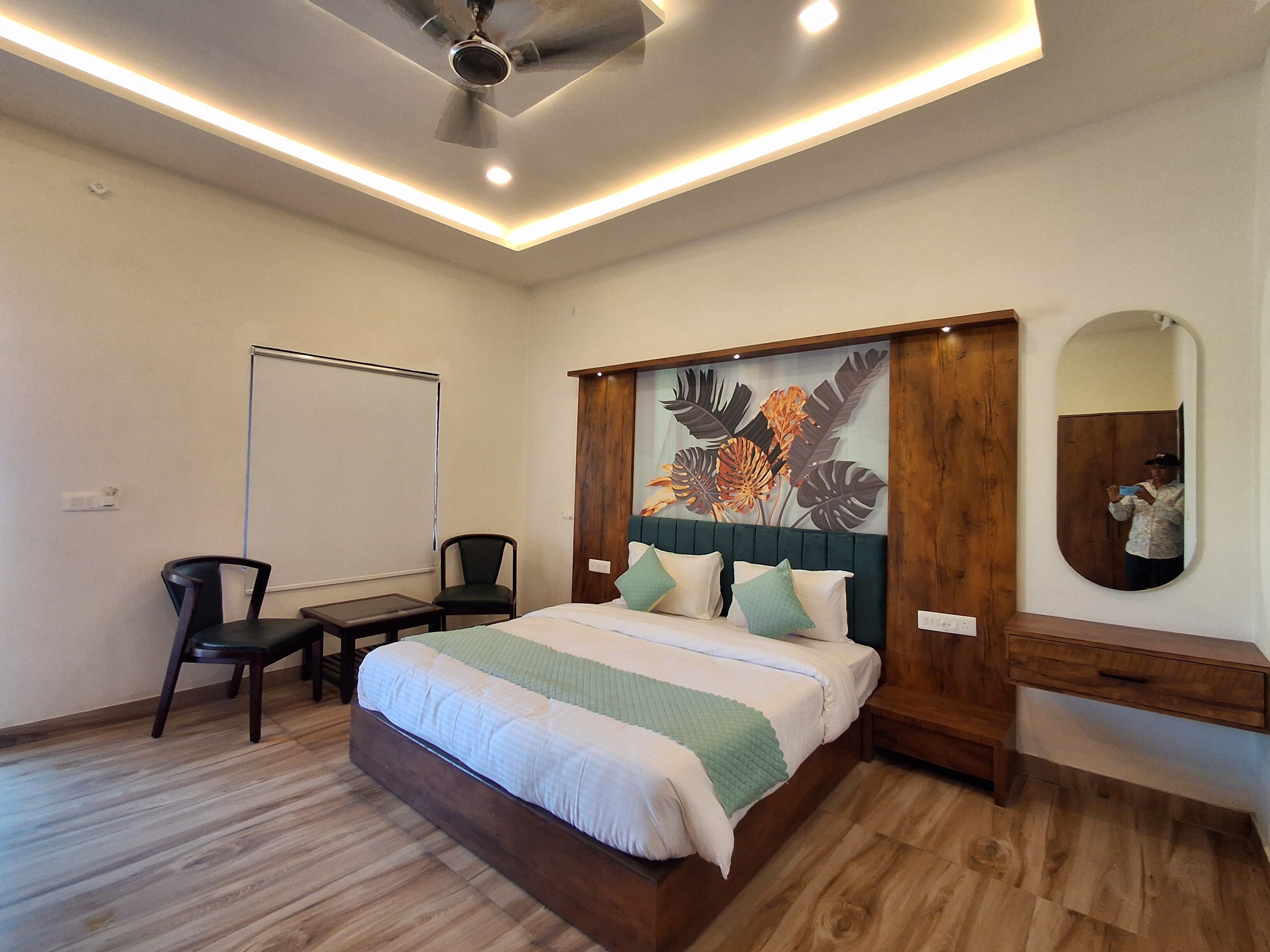 A bedroom with a bed, a desk, a chair, a ceiling fan, and a wall-mounted mirror.