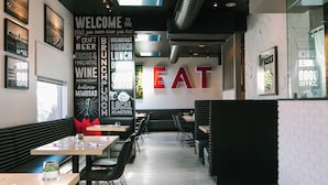 A modern restaurant interior with a central wall displaying the word "EAT" in large letters, surrounded by various food and drink options listed on the walls. - Solarena at Newport Beach (Newport Beach)