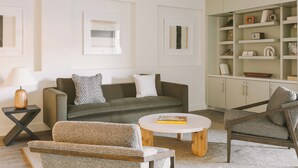 A modern living room with a sofa, armchair, coffee table, and a bookshelf. - Solarena at Newport Beach (Newport Beach)