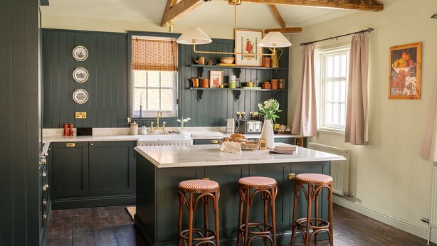 A kitchen with dark green cabinets, a white island with stools, wooden beams on the ceiling, and a window with curtains. - Chapman House - 3 Bedroom City Centre Retreat (Norwich)