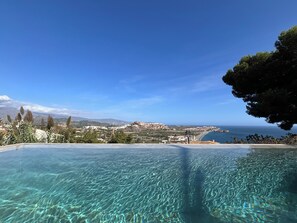 A clear view of a swimming pool with a scenic landscape in the background, including a coastline and distant mountains.