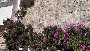 Ein modernes Haus mit einer Stein-Fassade, einem Balkon mit weißen Geländern und violetten Blumen im Vordergrund.