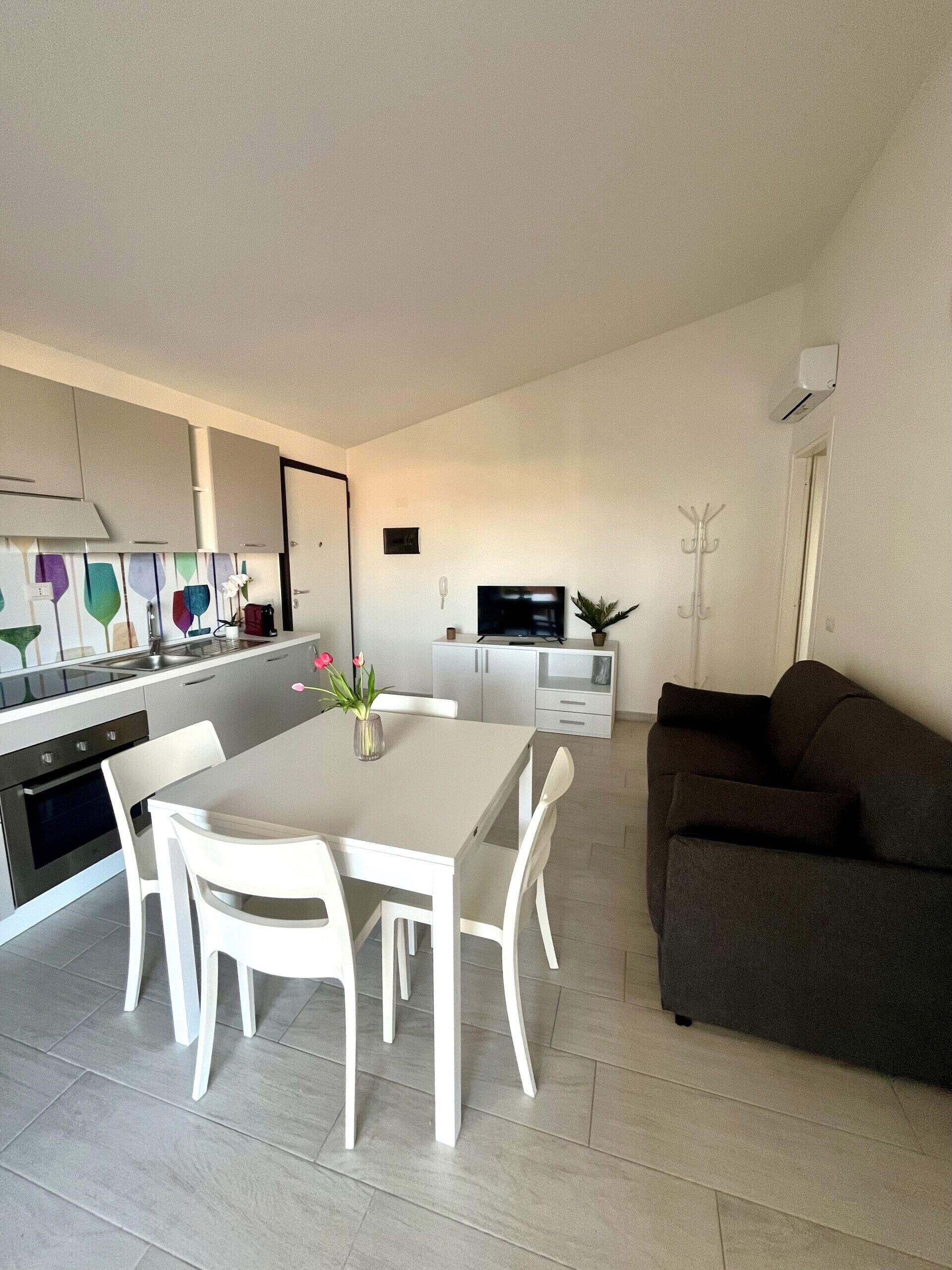 Une cuisine moderne avec des meubles blancs, une table à manger avec des chaises, un canapé foncé et un téléviseur en arrière-plan.