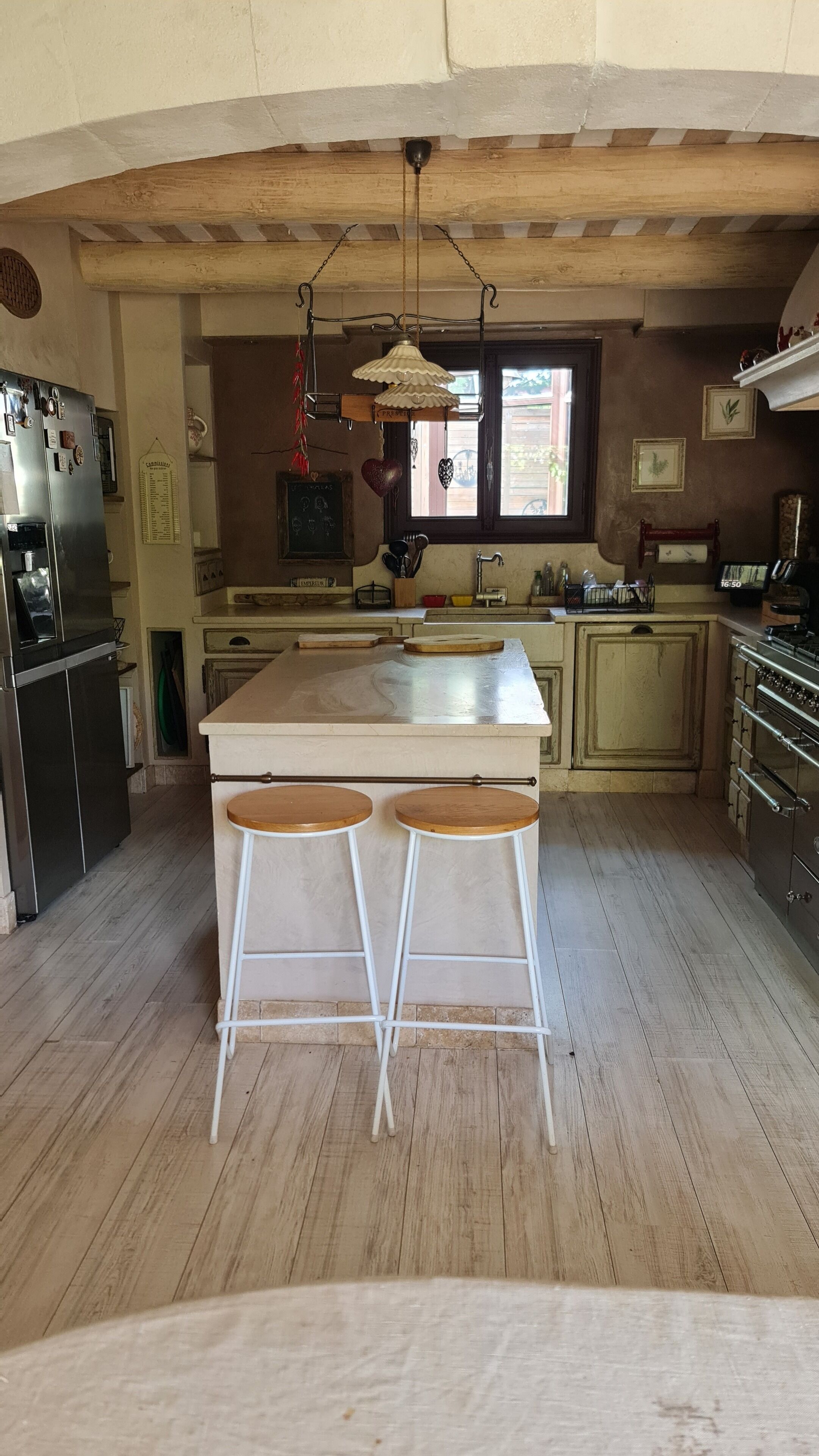 Una cocina con suelo de madera, una isla central con taburetes, una lámpara colgante y un ventanal con vistas.