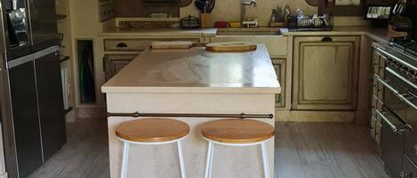 Una cocina con suelo de madera, una isla central con taburetes, una lámpara colgante y un ventanal con vistas.