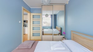 Un dormitorio con cama, un espejo, una mesita con una planta y vistas a una cocina y un pasillo.
