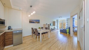 Una cocina moderna con lavavajillas, un comedor con mesa y sillas, un espacio de sala de estar con sofá y un amplio ventanal con cortinas.