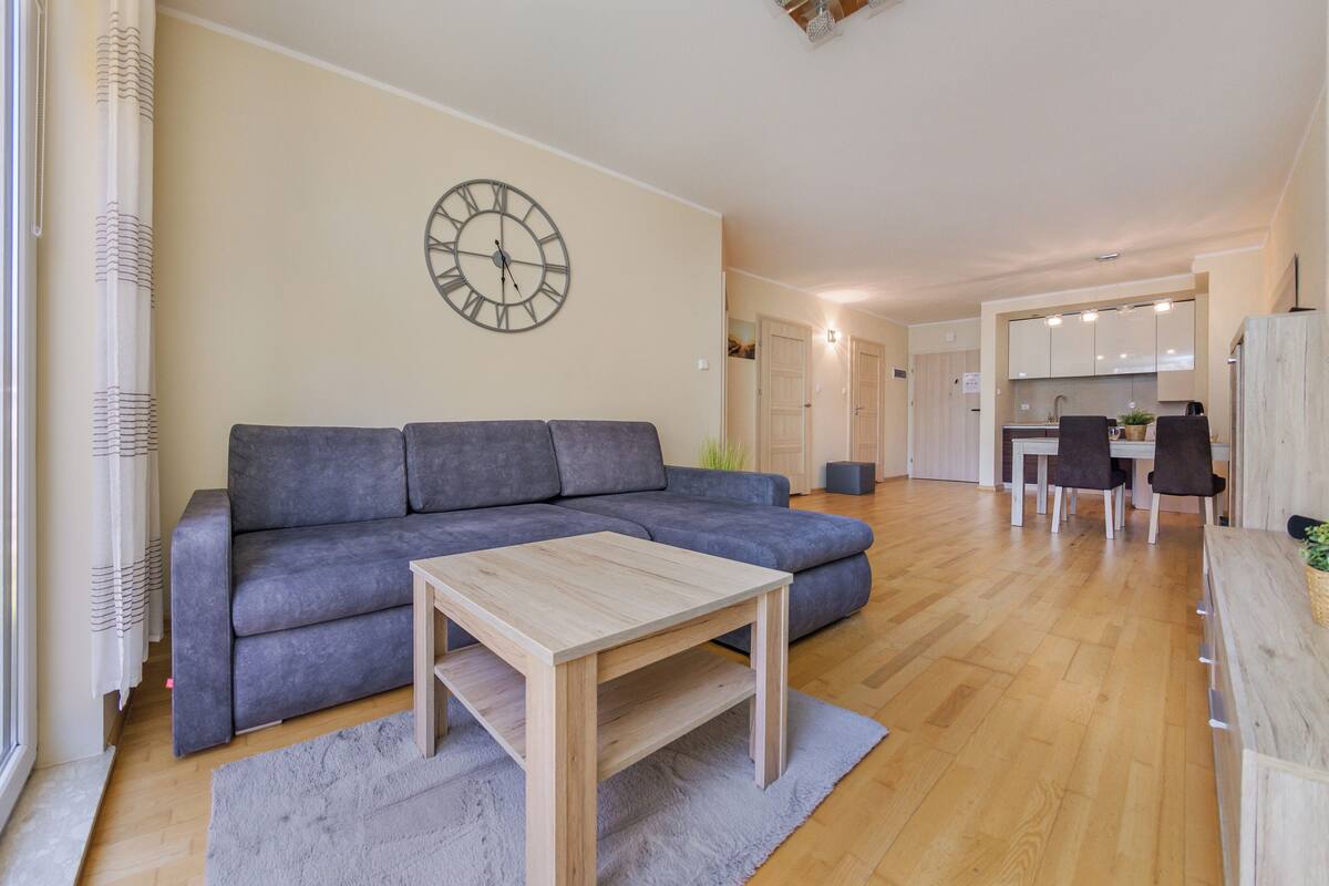 A modern living room with a grey sectional sofa, a wooden coffee table, and a wall clock.