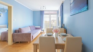 Una habitación de hotel moderna con una cama, un sofá, una mesa de comedor para dos personas y un gran ventanal con cortinas.