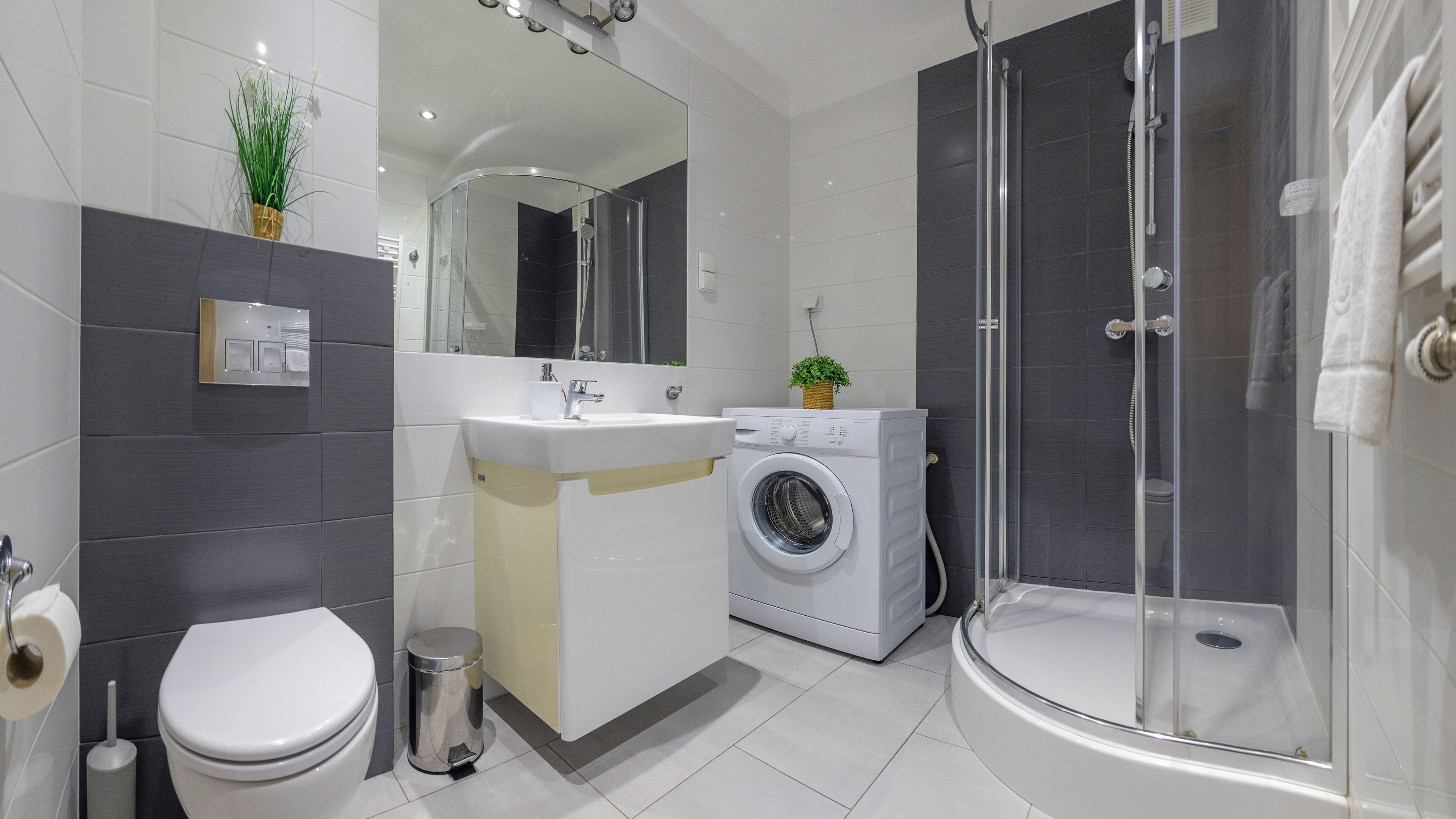 Ein modernes Badezimmer mit Toilette, Waschbecken, Waschmaschine und einer Duschkabine.