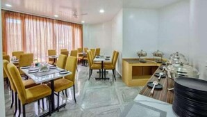 A dining area with multiple tables and chairs, a buffet station with food containers, and a ceiling fan. - Everest Hotel Manali (Manali)