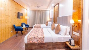 A hotel room with two beds, a wooden wall, a ceiling fan, a TV, and a small table with a lamp. - Everest Hotel Manali (Manali)