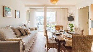 Een moderne woonkamer met een bank, eettafel en stoelen, een groot raam met uitzicht op de stad, en een hanglamp.