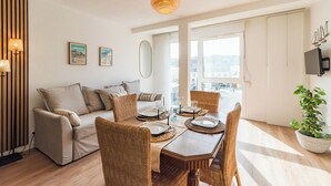 Een moderne woonkamer met een zithoek, een eettafel, rieten stoelen en een groot raam met uitzicht op de stad.