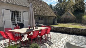 A patio with a table and chairs, a potted plant, and a house in the background.
