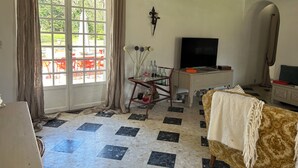 A room with a large window, a TV, a desk, and a patterned sofa.