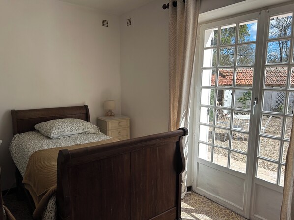 Une chambre à coucher avec un lit en bois, une table de chevet avec une lampe et une vue sur l’extérieur grâce à une porte vitrée.
