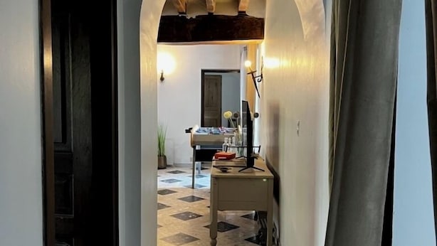 A narrow hallway with a tiled floor, an arched doorway, and a small table with items on it.