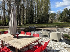 Un patio al aire libre con una mesa de madera y sillas rojas, rodeado de piso de piedra y una pared de piedra.