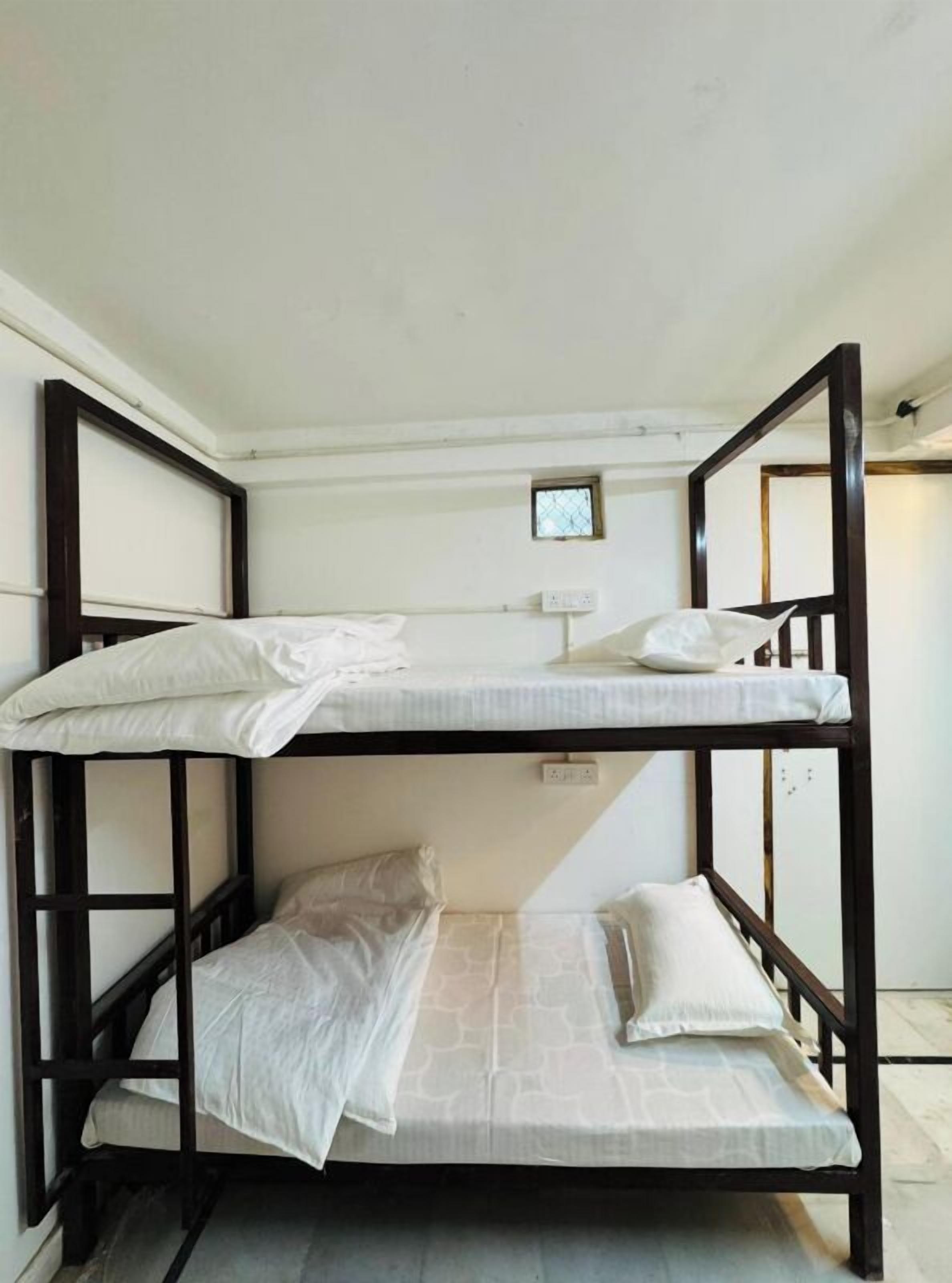 A bunk bed with three levels, white bedding, and a small window above the top bunk.