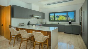 Een moderne keuken met een centraal eiland, barstoelen, een groot raam en ingebouwde apparatuur.