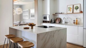 Una cocina moderna con una isla de mármol, taburetes de madera, horno empotrado y una lámpara colgante.