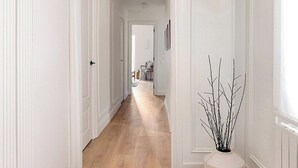 Un pasillo con suelo de madera, paredes blancas y una puerta blanca al final.