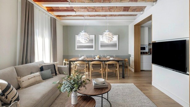 Una sala de estar moderna con techo de ladrillo, una zona de comedor con sillas de madera, un sofá con cojines, una mesa de centro y un televisor de pantalla plana.