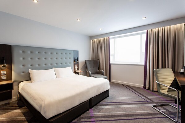 Habitación de hotel con una cama grande, un escritorio, una silla, una mesita de noche y una ventana con cortinas.