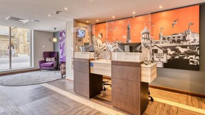A hotel reception desk with a large window, a purple chair, and a wall with a cityscape mural. - Premier Inn Blackpool - North Pier (Blackpool)