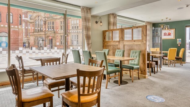 A hotel lobby with large windows, wooden tables, and green upholstered chairs. - Premier Inn Blackpool - North Pier (Blackpool)