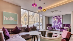 A modern hotel lobby with a large window, a 'hello' sign, purple and beige furniture, and a purple wall art piece. - Premier Inn Blackpool - North Pier (Blackpool)