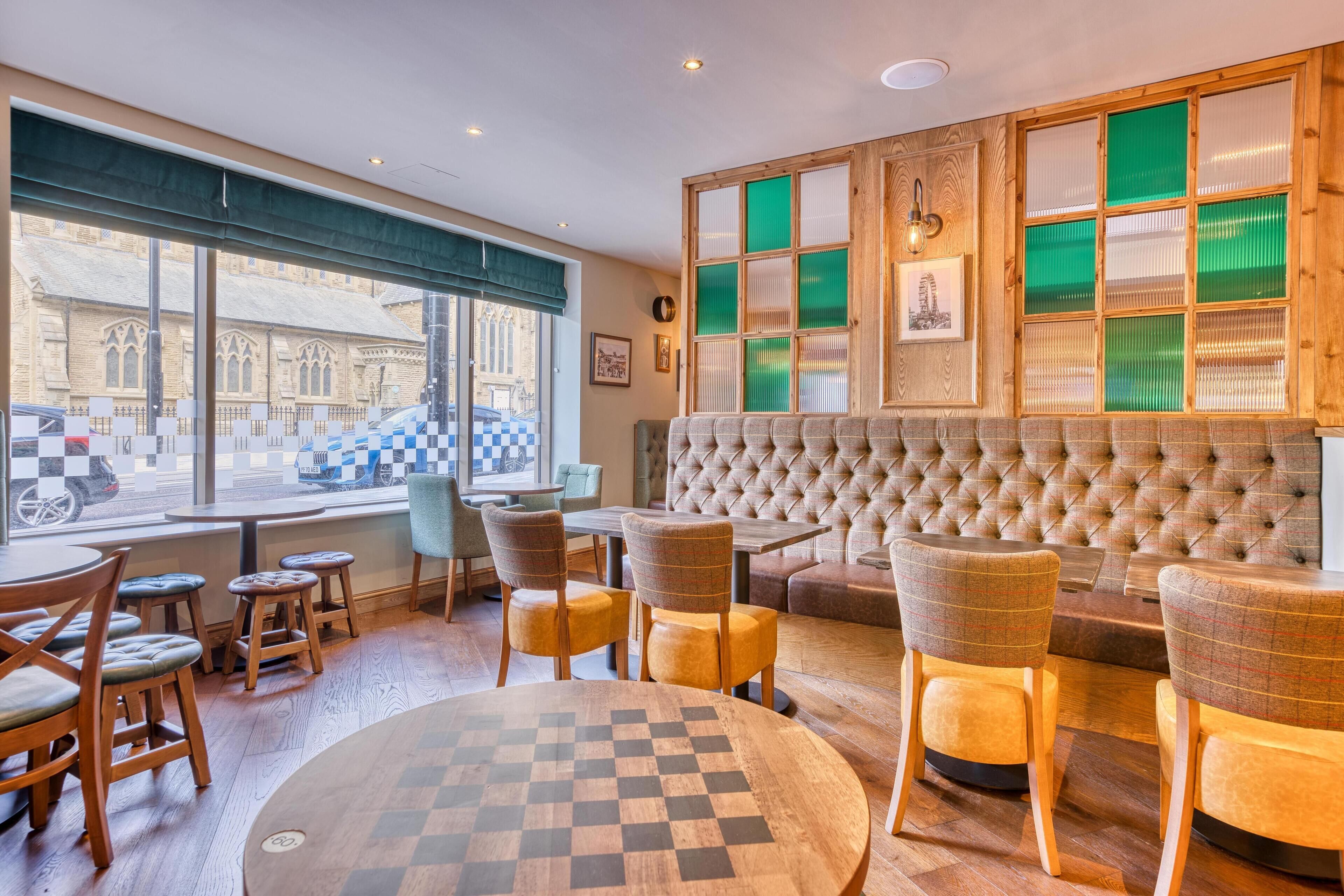 A cozy cafe with a checkered table, cushioned seating, and large windows overlooking a street.