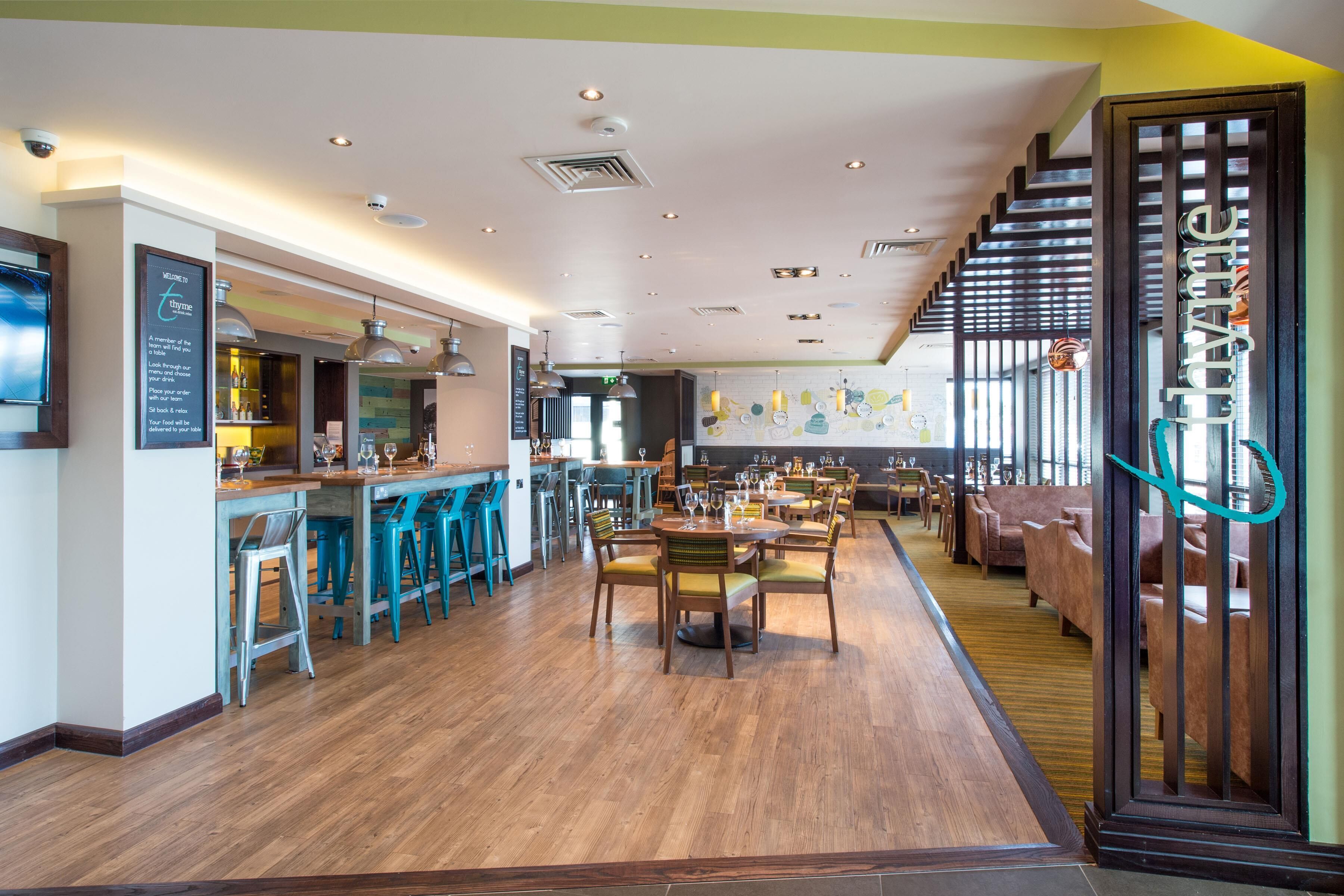 Un amplio bar con taburetes altos, una zona de estar con mesas y sillas, y una escalera que conduce a un nivel superior.