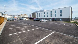 Un parking avec des places délimitées, un bâtiment moderne doté de nombreuses fenêtres et un ciel dégagé.