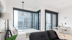 A modern bedroom with a bed, a black sofa, a desk, and large windows. - RentPlanet - Apartament Prosta (Warsaw)