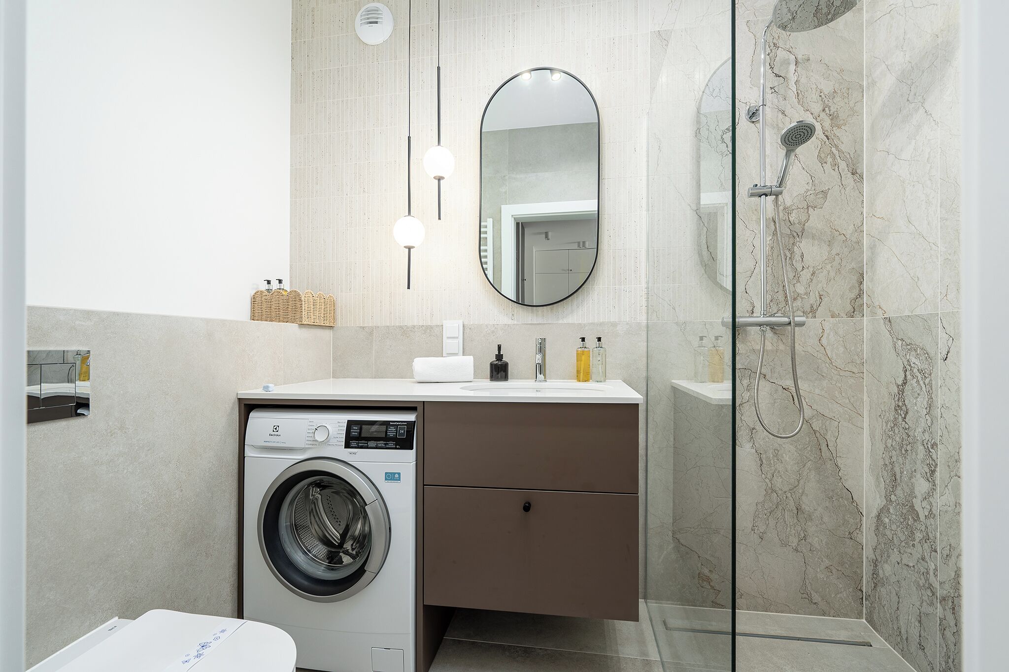 Ein modernes Badezimmer mit Waschmaschine, Spiegel, Dusche und Waschbecken mit Pflegeprodukten.