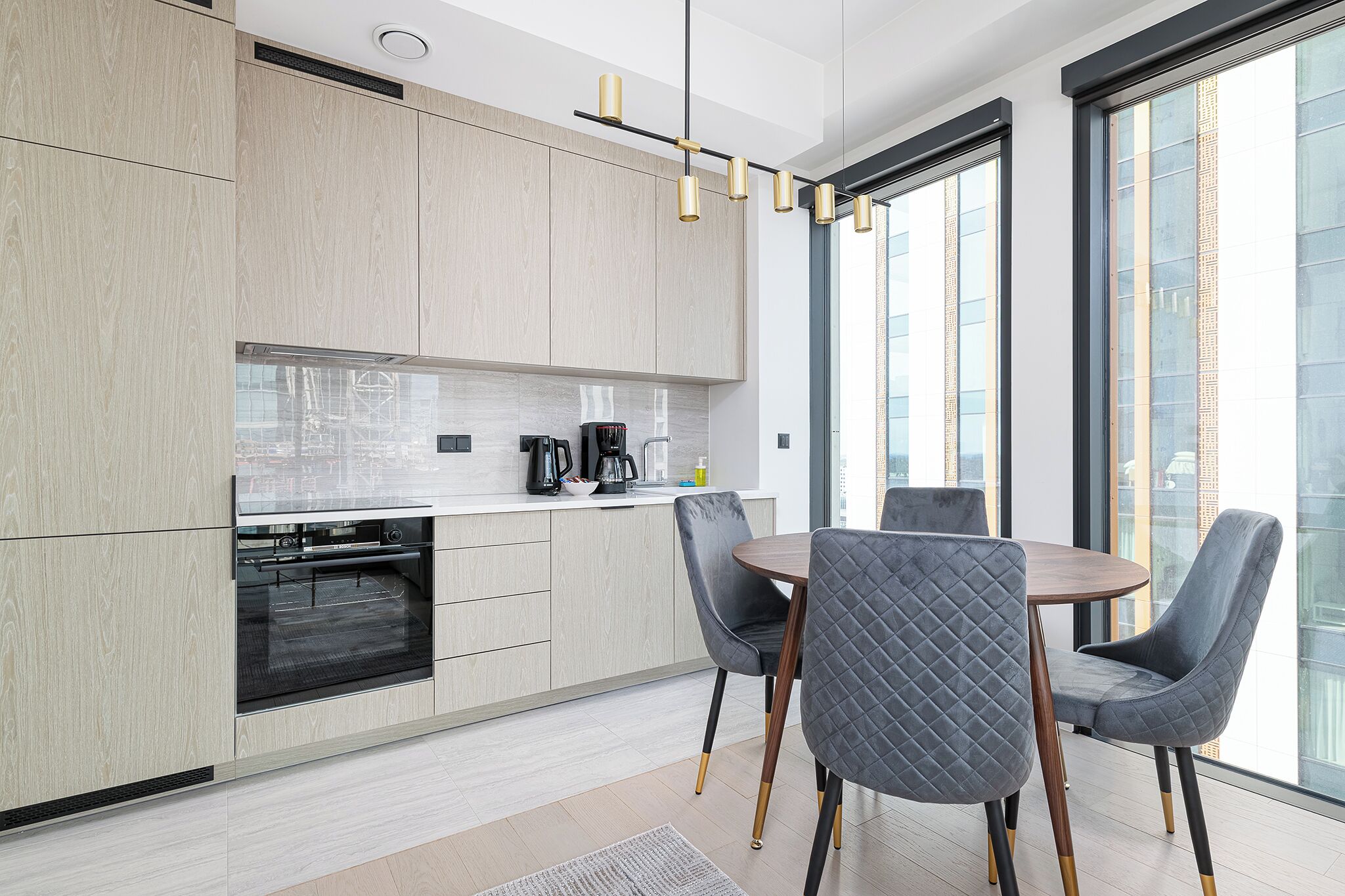 Una cocina moderna con electrodomésticos integrados, una zona de comedor con dos sillas y ventanas grandes que ofrecen vistas a la ciudad.