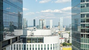 A high-rise building with a modern glass facade, surrounded by other skyscrapers, and a clear sky with clouds. - RentPlanet - Apartament Prosta (Warsaw)