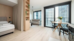 A modern bedroom with a bed, a wooden wardrobe, a sofa, and a dining area with a table and chairs. - RentPlanet - Apartament Prosta (Warsaw)
