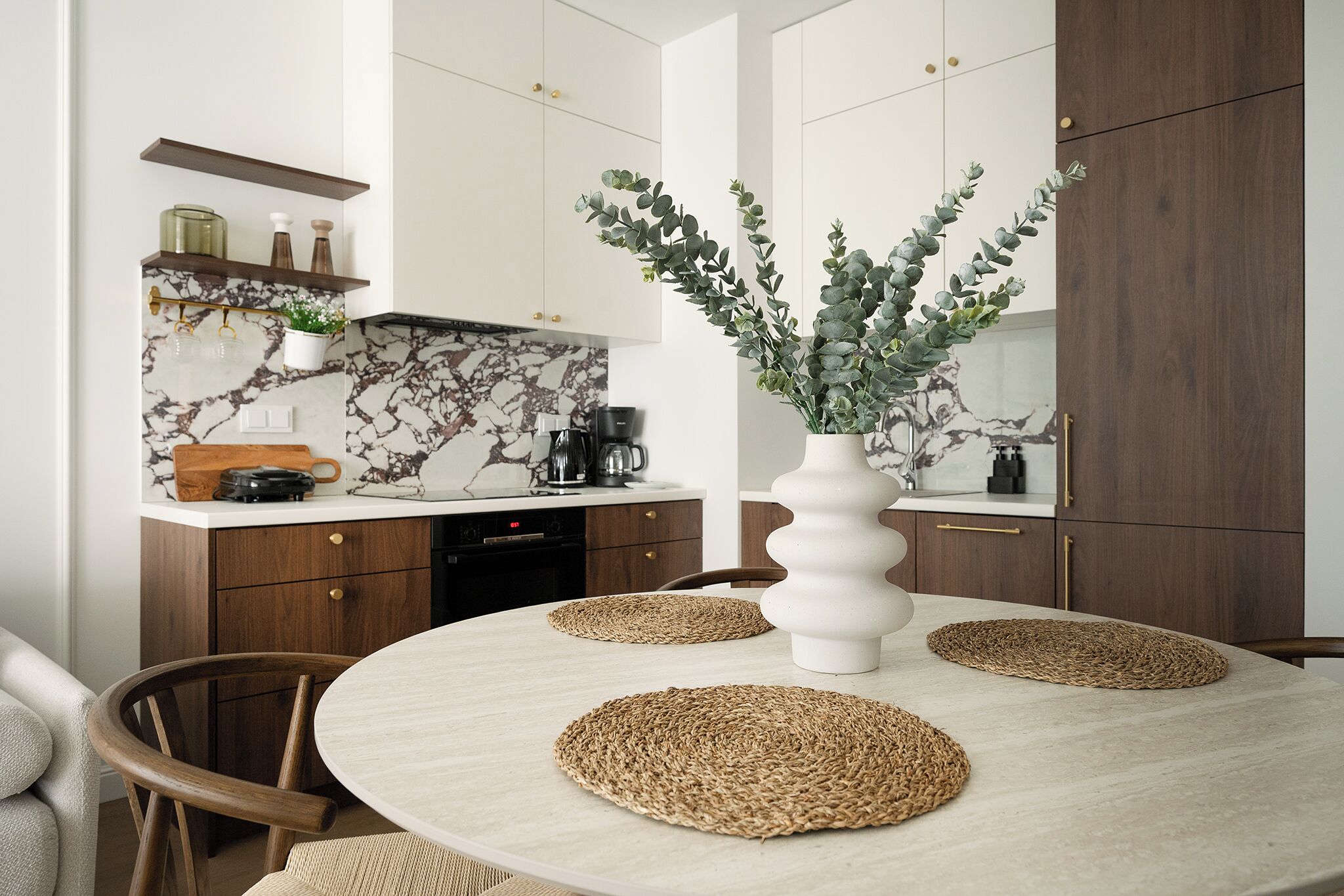 A modern kitchen with marble countertops, wooden cabinets, and a central island with a vase of greenery.