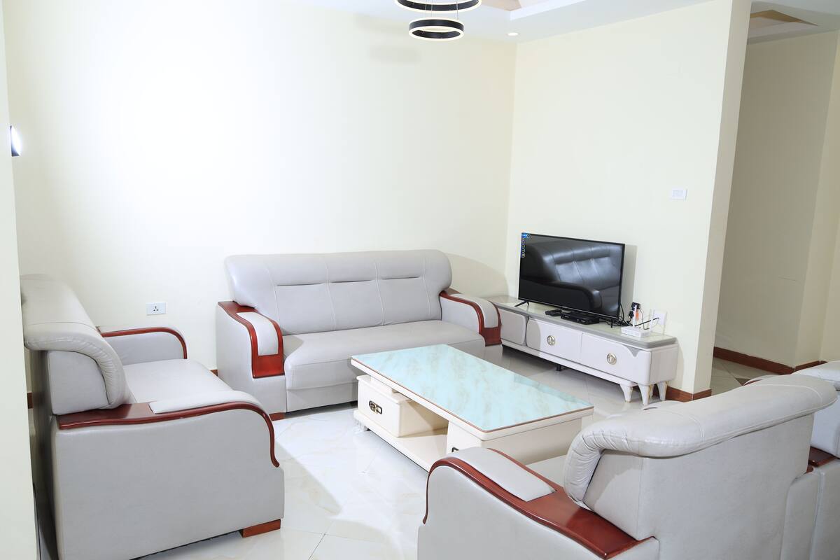 A modern living room with a sofa, armchairs, a coffee table, and a TV.