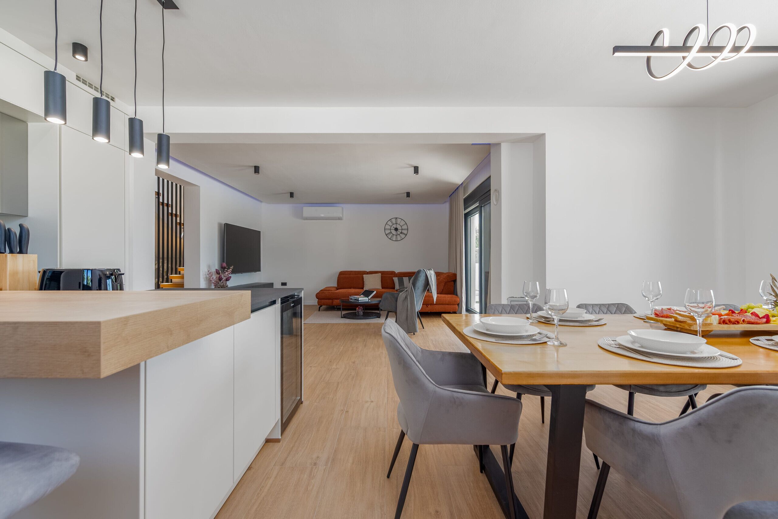 Una cocina moderna con encimera de madera, un comedor con mesa y sillas de madera, y una sala de estar con sofá y televisor.