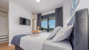 A modern hotel room with a large bed, a flat-screen TV mounted on the wall, and a view of the outdoors through a large window. - Villa Roma Murvica Zadarvillas (Policnik)