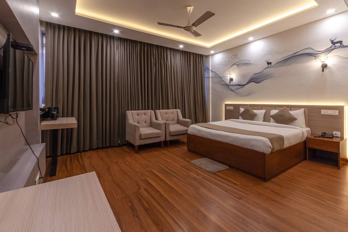 A modern hotel room with a large bed, two armchairs, a desk, and a ceiling fan.