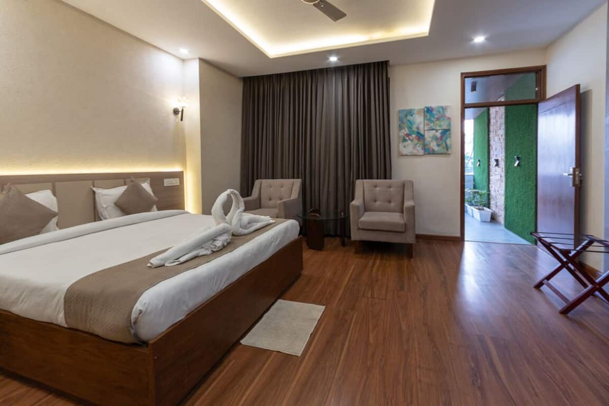 A modern hotel room with a large bed, two armchairs, a small table, and a green wall.