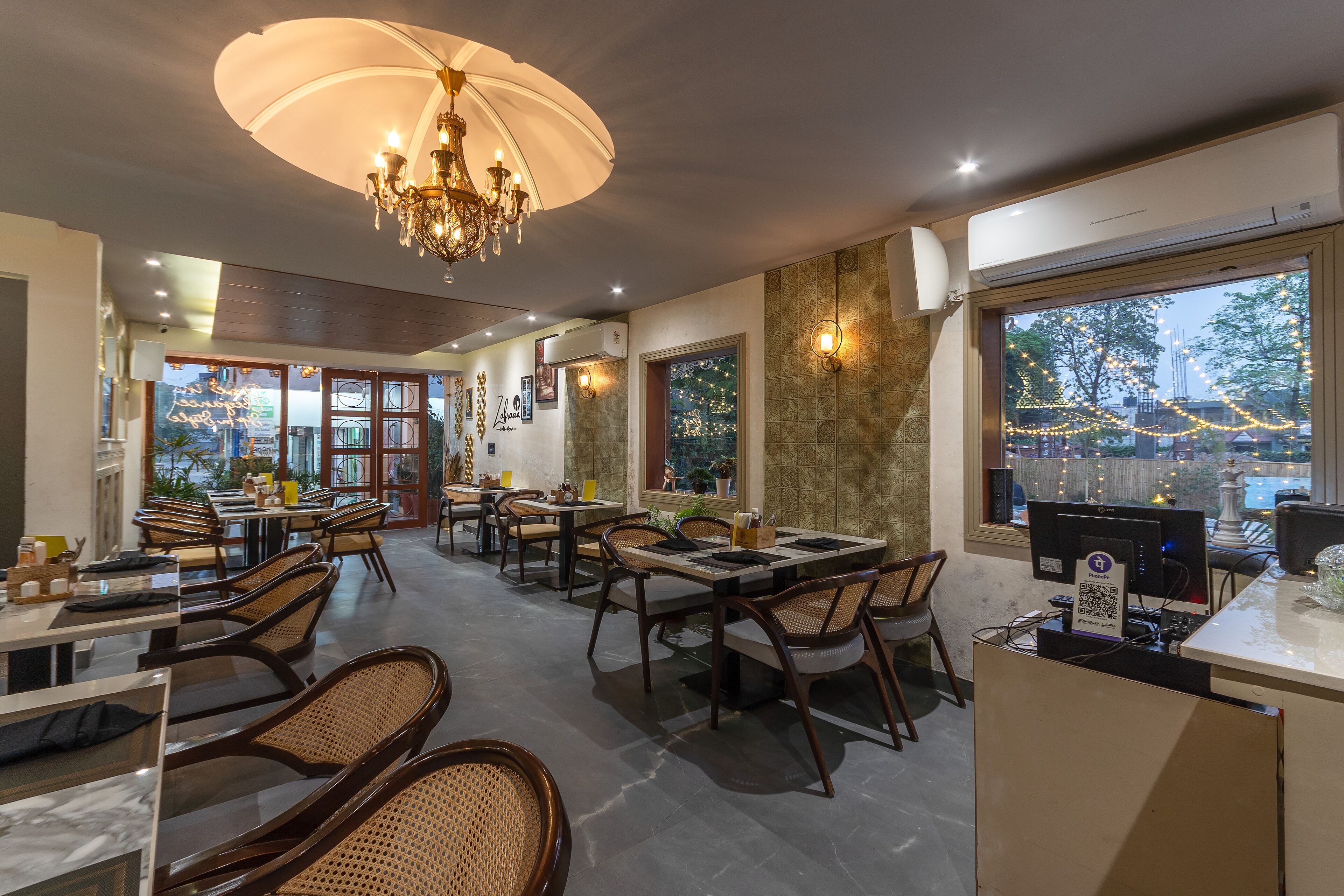 A restaurant with tables and chairs, a chandelier, and a view through the windows.
