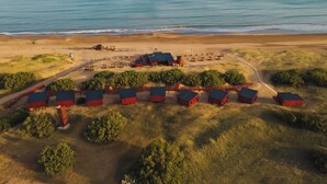 An aerial view of a coastal property with multiple red-roofed buildings, a beach, and a clear view of the ocean. - AV366 (Arenas Verdes)