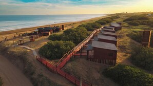 A coastal property with a wooden deck leading to a series of cabins, a beach, and a clear sky. - AV366 (Arenas Verdes)