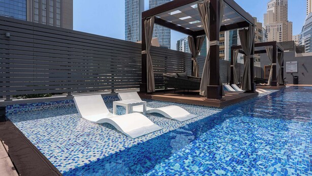 Ein Pool auf dem Dach mit Liegestühlen und einer Pergola, umgeben von Hochhäusern.